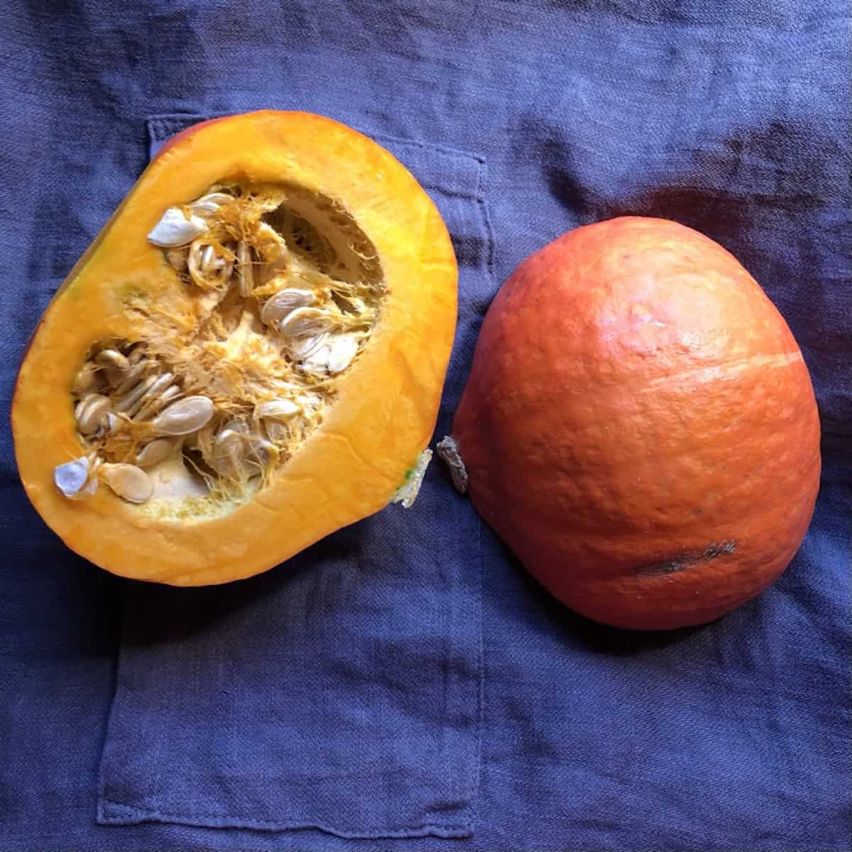 Fresh hokkaido pumpkin cut in half showing flesh and seeds and the one half showing the skin for homemade pumpkin pie recipe, pumpkin cheesecake, pumpkin puree, pumpkin bread, but not an ingredient in pumpkin pie spice.