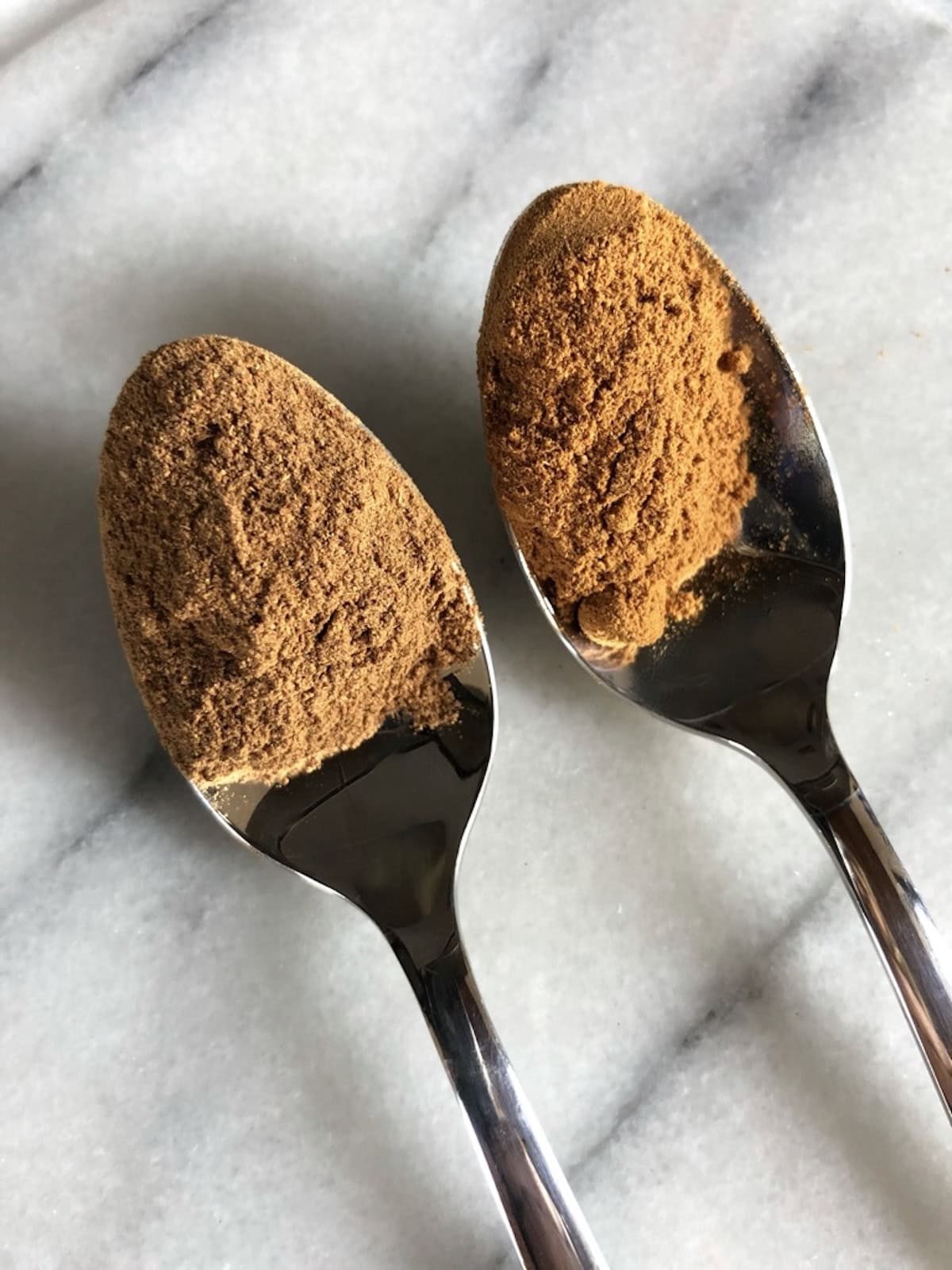 Copycat pumpkin pie spice recipe comparison with McCormick brand on marble dish, homemade pumpkin spice substitute ingredients in spoons, what is in pumpkin pie spice blend mix.