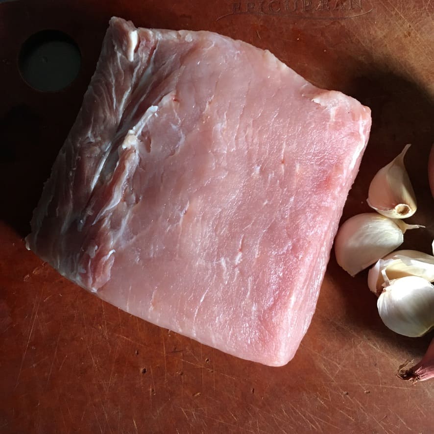 a piece of raw pork loin on the cutting board next to garlic cloves