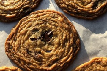 a parchment lined sheet tray with just baked pan banger chocolate chip cookies with beautiful ridges all the way around multiple times from the middle to the edges like the ripples made when you skip rocks across a pond