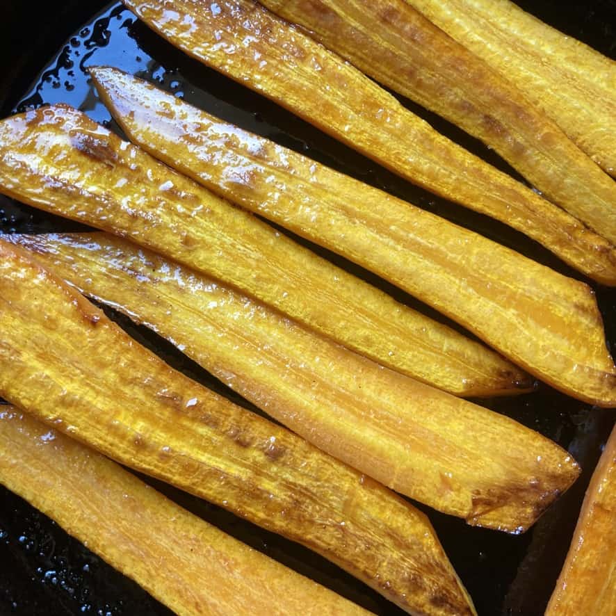 perfectly pan seared long carrot slices glistening with olive oil in cast iron skillet
