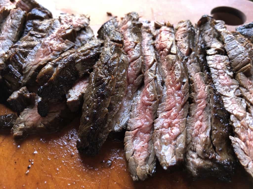 perfectly pan seared flank steak sliced and lying in a row on a cutting board revealing the crusty outside and pink middles