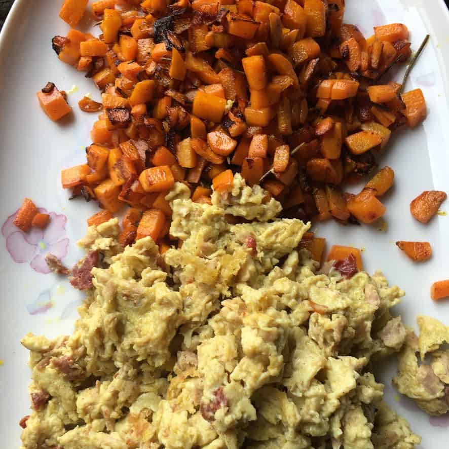 a platter filled diced sauteed golden carrots on on end and scrambled eggs with crispy prosciutto on the opposite end