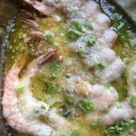 a shallow platter with perfectly cooked tender shrimp scampi with butter and olive oil, sliced scallions and parsley