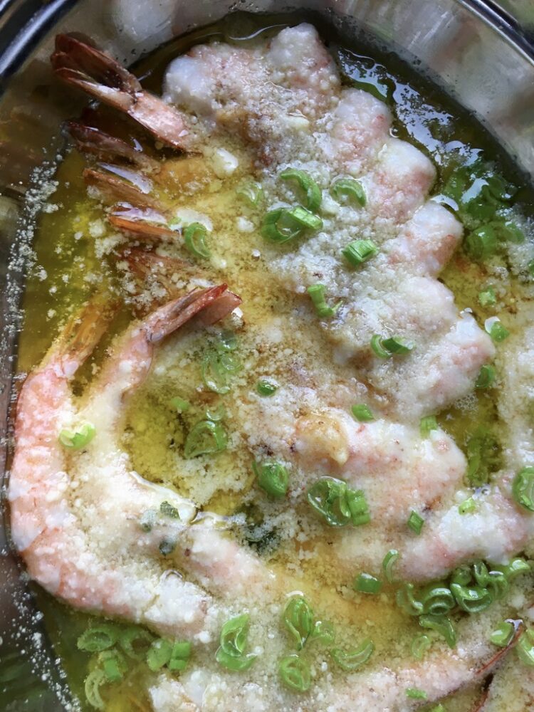 a shallow platter with perfectly cooked tender shrimp scampi with butter and olive oil, sliced scallions and parsley
