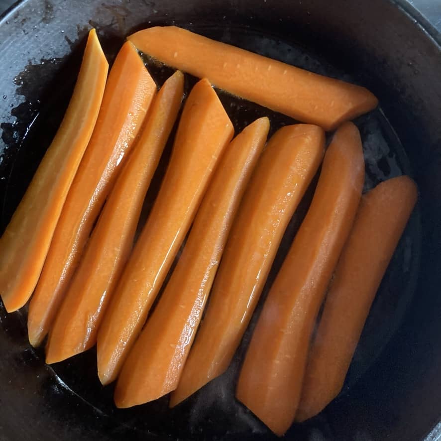 halved carrots lined up in an olive oiled cast iron skillet (flat side down)
