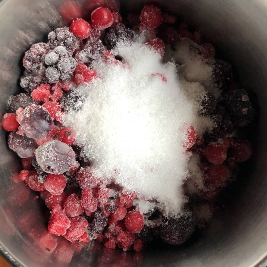 a view into a pot with frozen mixed berries (raspberries, blueberries, currants, and blackberries) and lemon juice and sugar in the middle