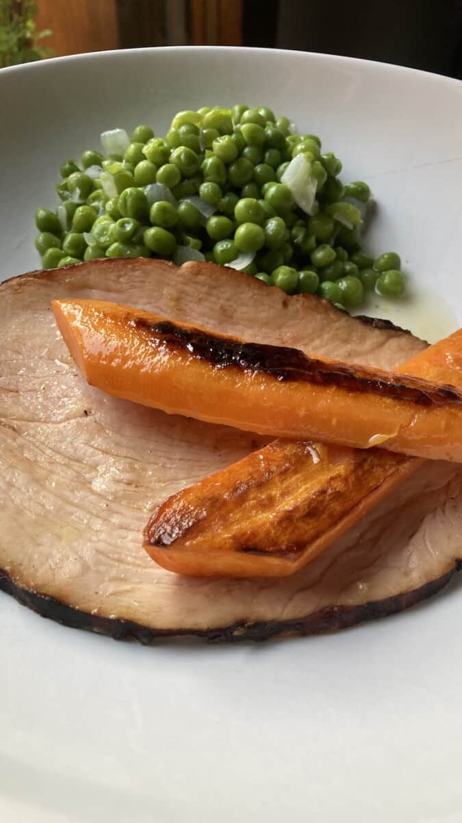 2 pieces of pan seared carrots criss-crossed over each other lying on top of a piece of roast turkey breast with a side of peas on a plate