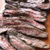 perfectly pan seared flank steak sliced and lying in a row on a cutting board revealing the crusty outside and pink middles