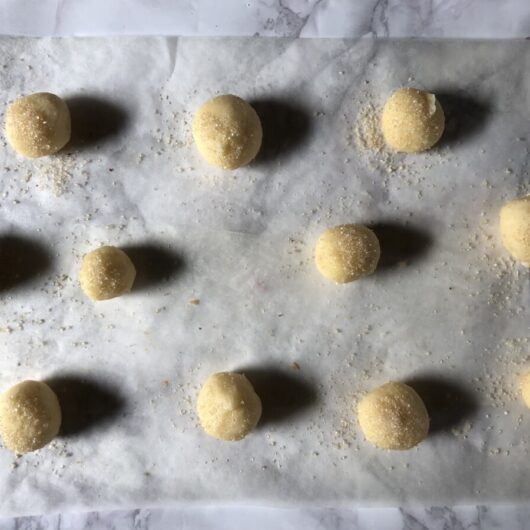 parchment paper-lined cookie sheet with 11 raw sugar cookie dough balls