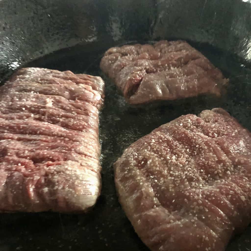 flank steaks in a cast iron skillet pan searing
