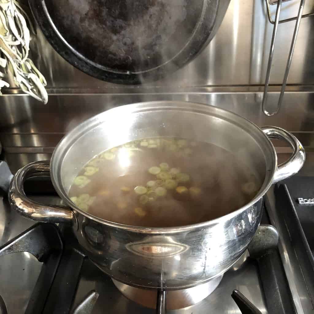 simmering egg drop soup base with scallions floating on top
