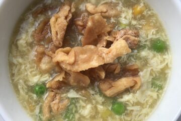 a small bowl of egg drop soup with crispy fried homemade wonton strips, green peas, corn, and sliced scallions