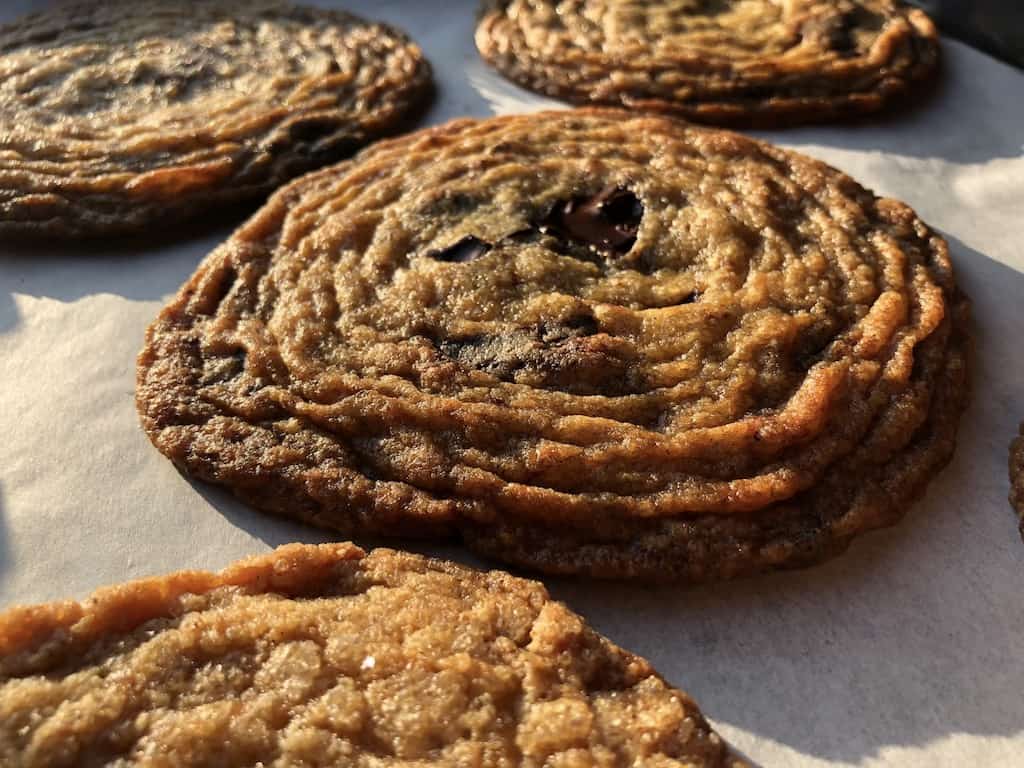 a parchment lined sheet tray with just baked pan banger chocolate chip cookies with beautiful ridges all the way around multiple times from the middle to the edges like the ripples made when you skip rocks across a pond