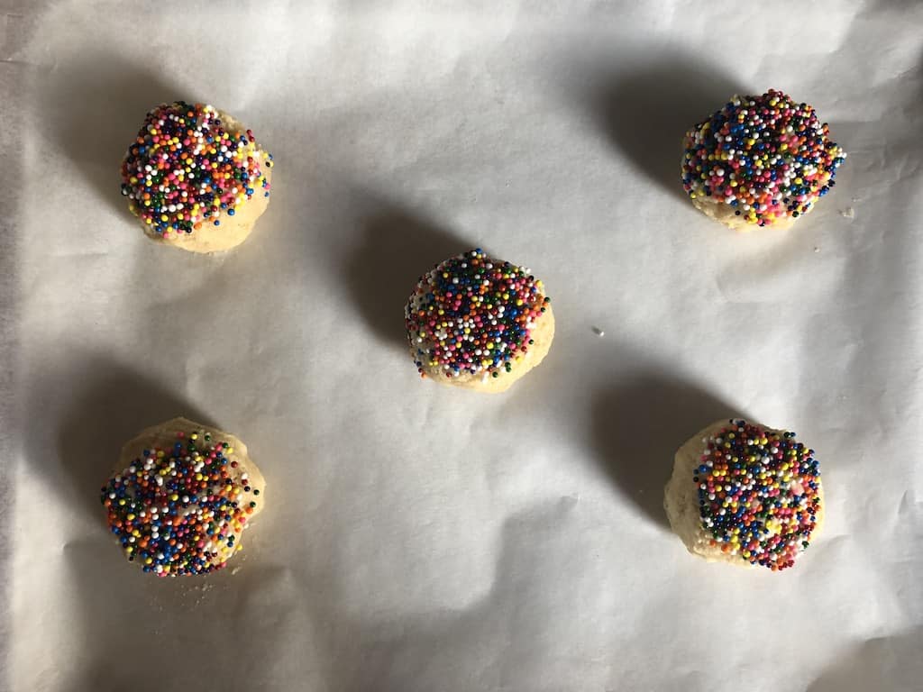 a sheet pan lined with white parchment paper with raw sugar cookie dough balls with nonpareil sprinkles