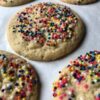 a sheet pan lined with white parchment paper with freshly baked sugar cookies with nonpareil sprinkles