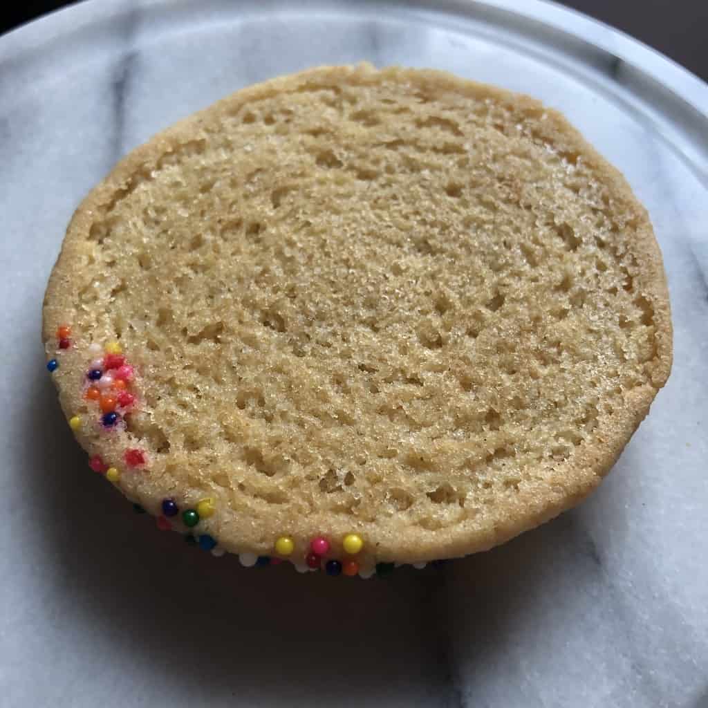 the bottom side of the perfectly baked "blonde" sugar cookie with a little hot pink nonpareil around the bottom left edge