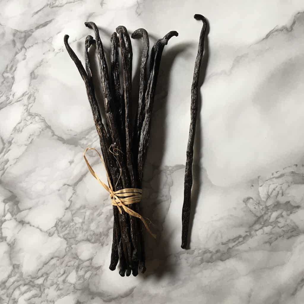vanilla beans in a bundle tied with raffia and one single bean off to the right