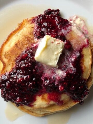 A stack of fluffy pancakes with a wedge removed showing the light airy interior of these homemade buttermilk pancakes.