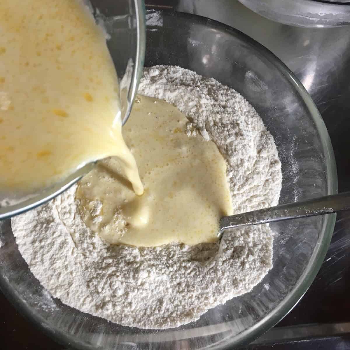 Wet ingredients added to the dry ingredients in a mixing bowl for pancakes for two.