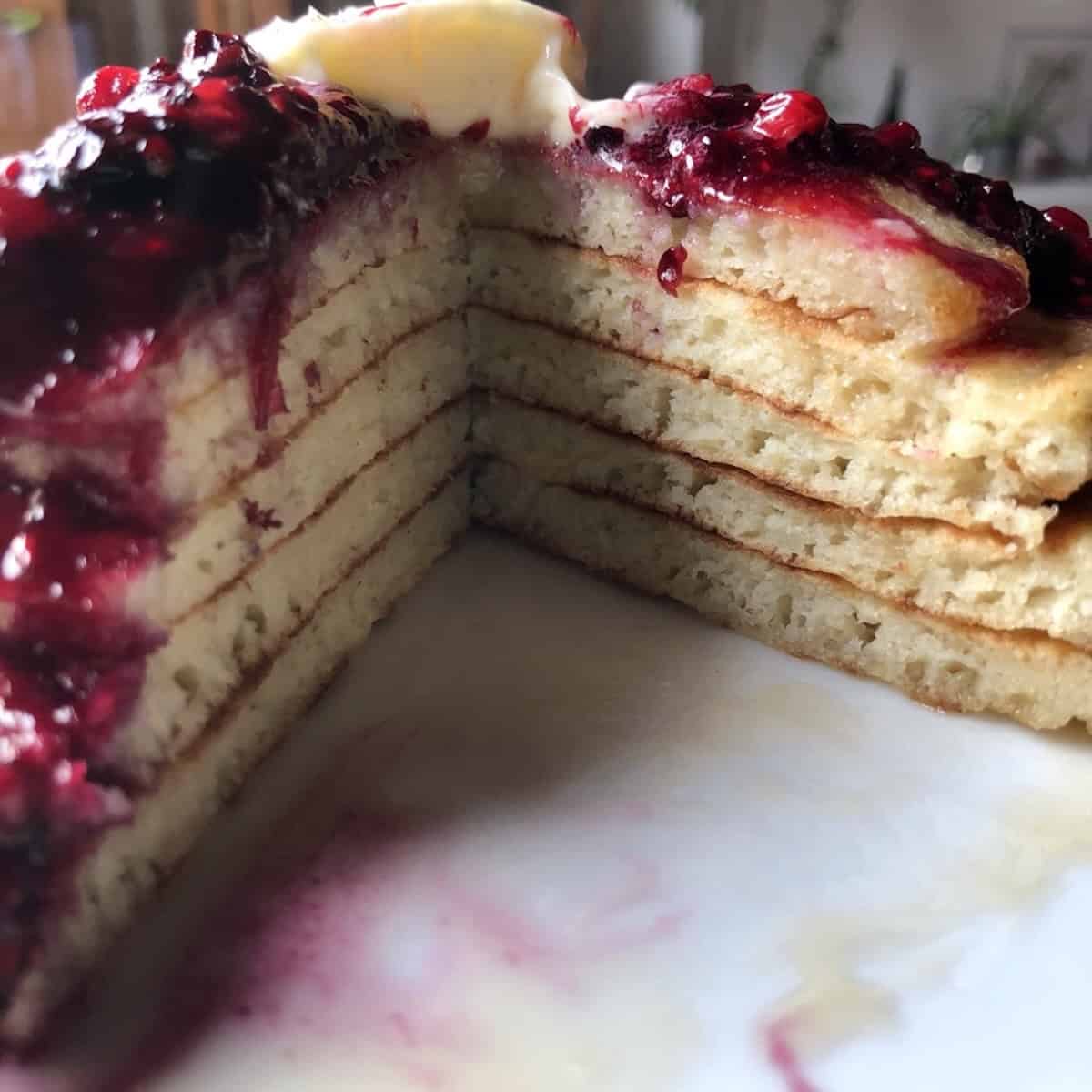 A stack of fluffy pancakes with a wedge removed showing the light airy interior of homemade buttermilk pancakes.