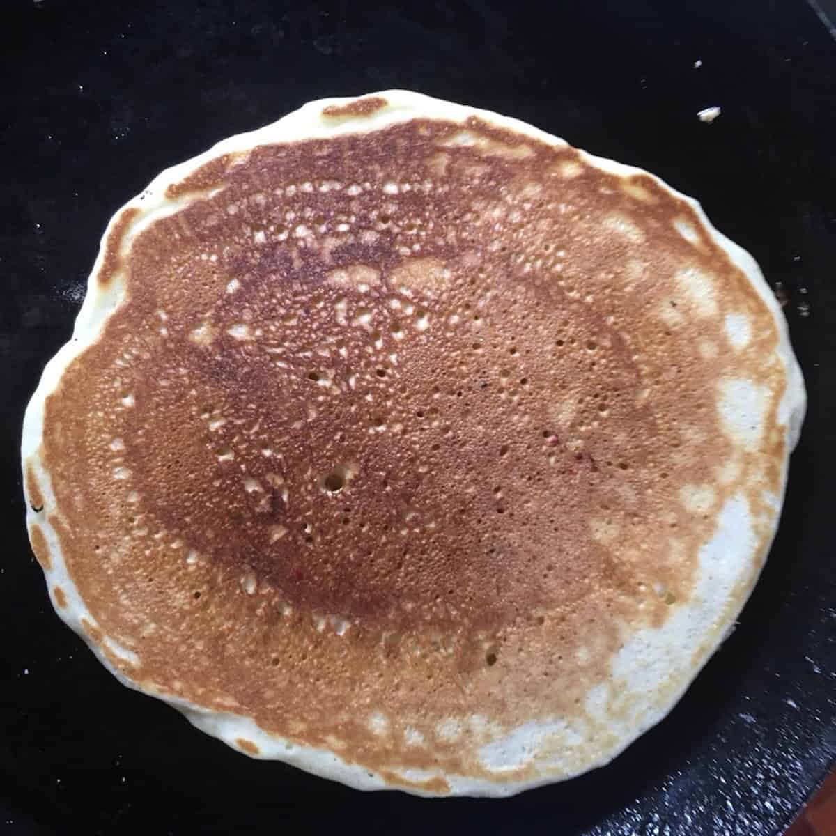 A perfectly golden brown pancake after being flipped at the right moment in the skillet.