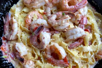 the most delicious creamy shrimp alfredo pasta ready to eat with huge red Argentinian shrimp on top of a zigzag regional egg pasta
