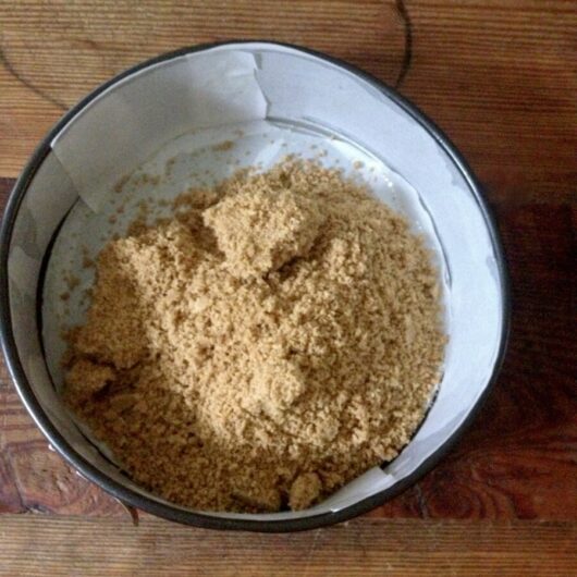 graham cracker crust mixture piled into a parchment-lined springform pan