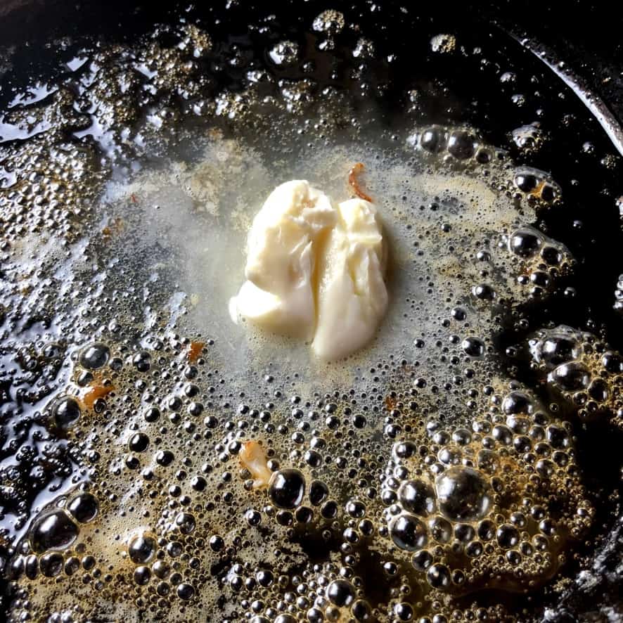 butter melting in a cast iron skillet bubbling and with visible orange and red bits left from the pan seared red shrimp
