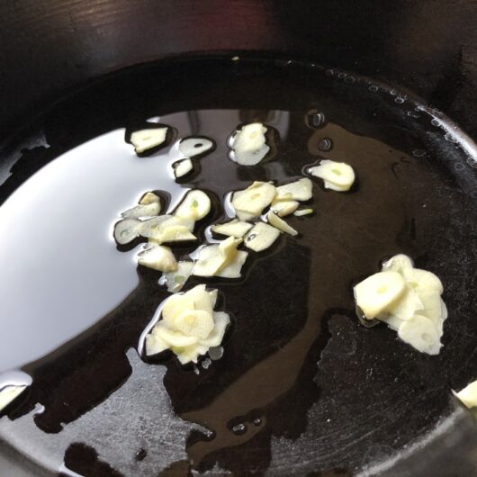 paper thin sliced garlic in one tablespoon of olive oil cooking in a cast iron skillet