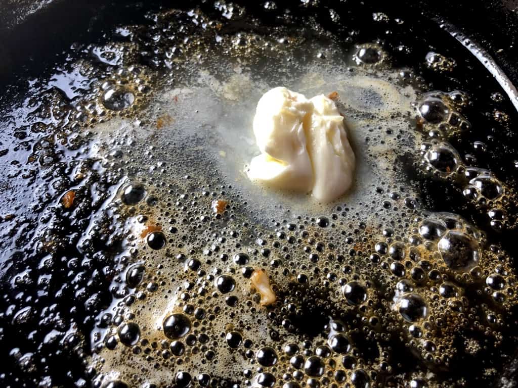 butter melting in a cast iron skillet bubbling and with visible orange and red bits left from the pan seared red shrimp