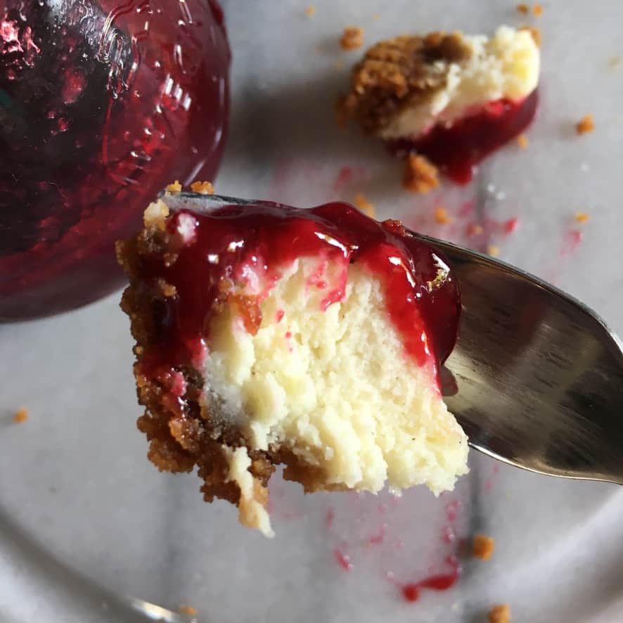 a perfect fluffy bite of vanilla bean cheesecake on a fork drizzled with deep red smooth berry sauce