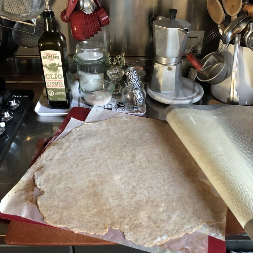 Showing a st. louis no yeast whole wheat pizza crust rolled out and added to a piece of parchment paper to be topped and easily transported to a preheated baking sheet in the oven. This is the best method if you don't have a pizza peel.