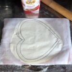 a piece of parchment paper placed on top of the rolled out dough and a heart shape drawn on it