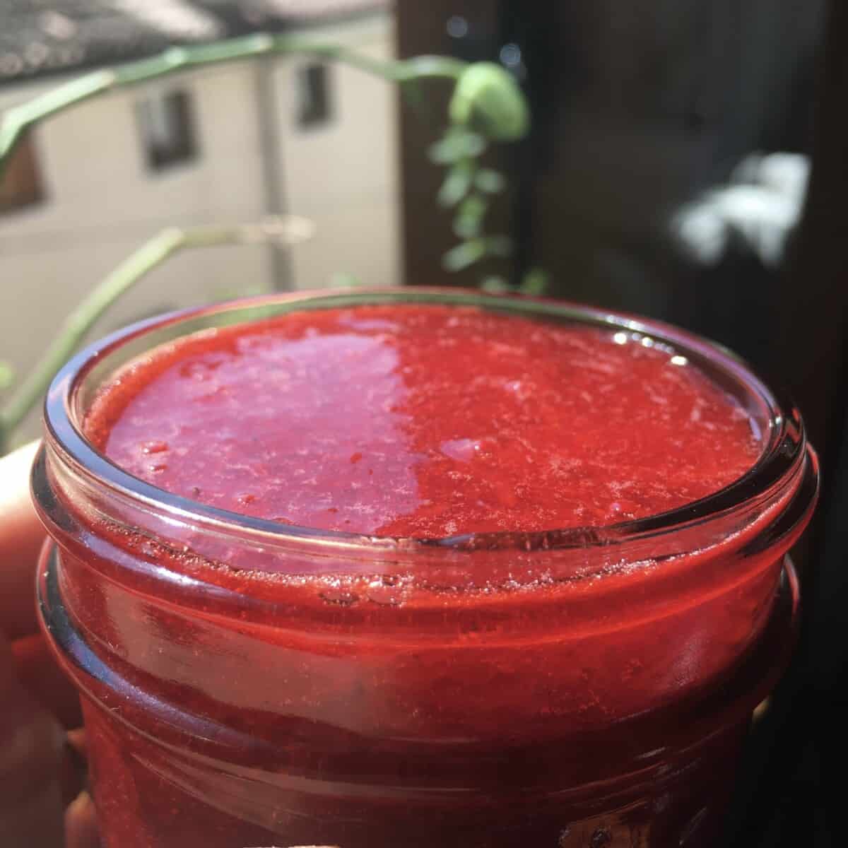 strawberry sauce in a small Mason jar looking super bright red with a view out of the window