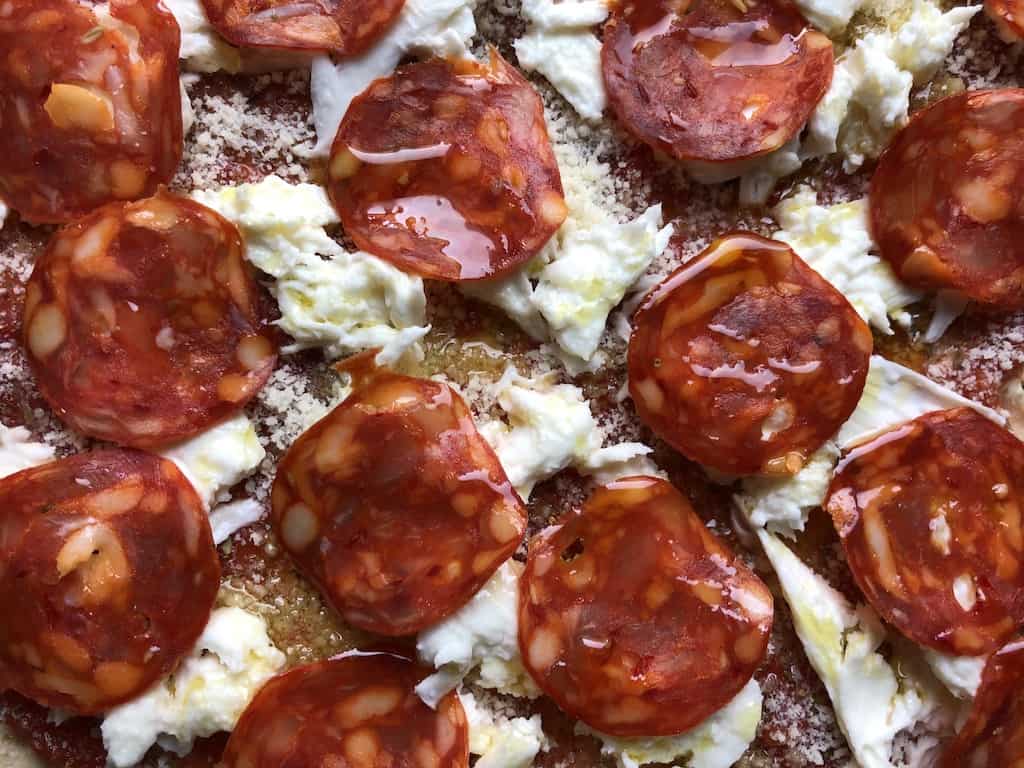 closeup of a sauced and topped pizza (showing toppings only : mozzarella freshly torn and pepperoni slices drizzled with olive oil just before being baked