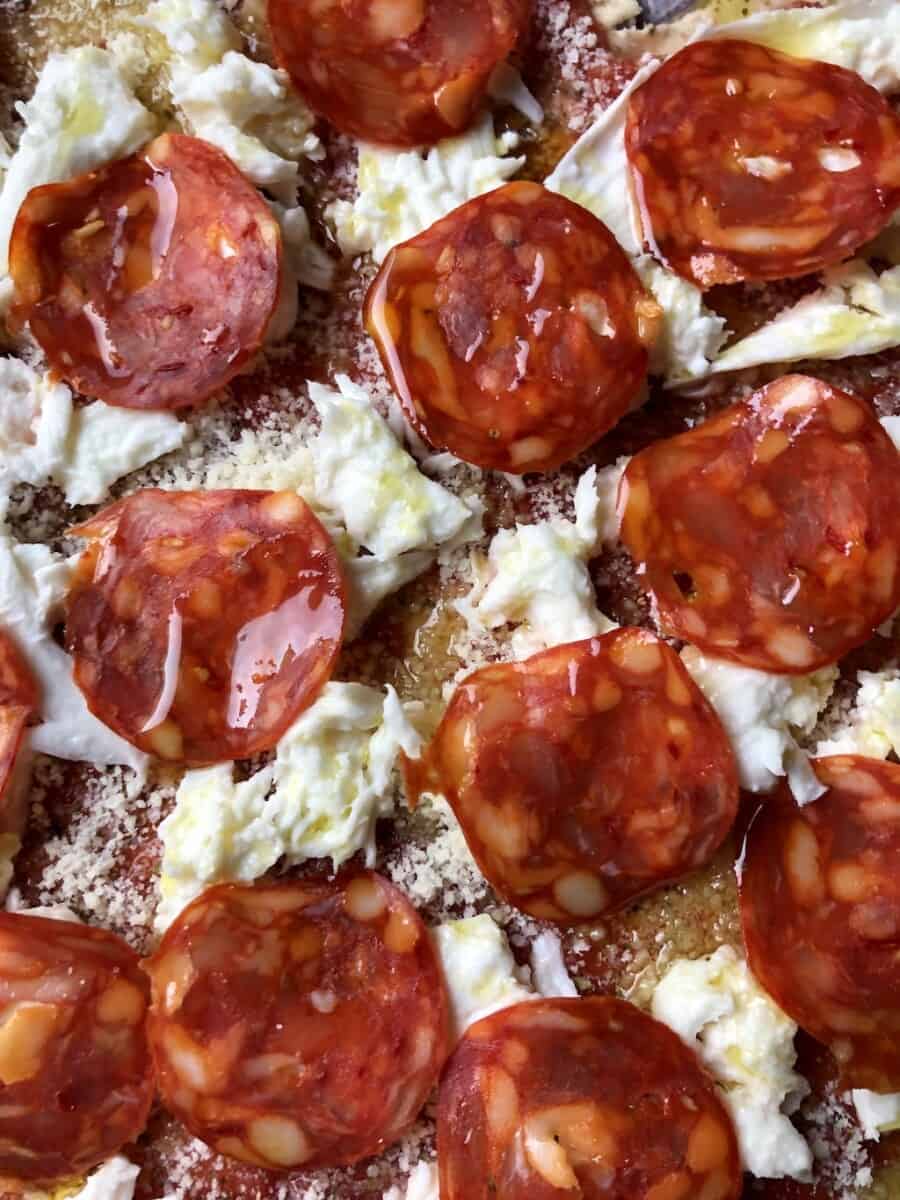 closeup of a buffalo mozzarella and pepperoni pizza drizzled with olive oil just before baking