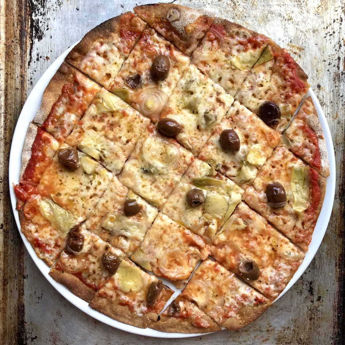 St. Louis style thin crust whole wheat pizza cut into squares topped with artichoke hearts, Taggiasche olives, caramelized onions and melted mozzarella cheese - no yeast pizza dough recipe.