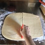 my hand splitting the dough into equal parts using a red plastic dough cutter