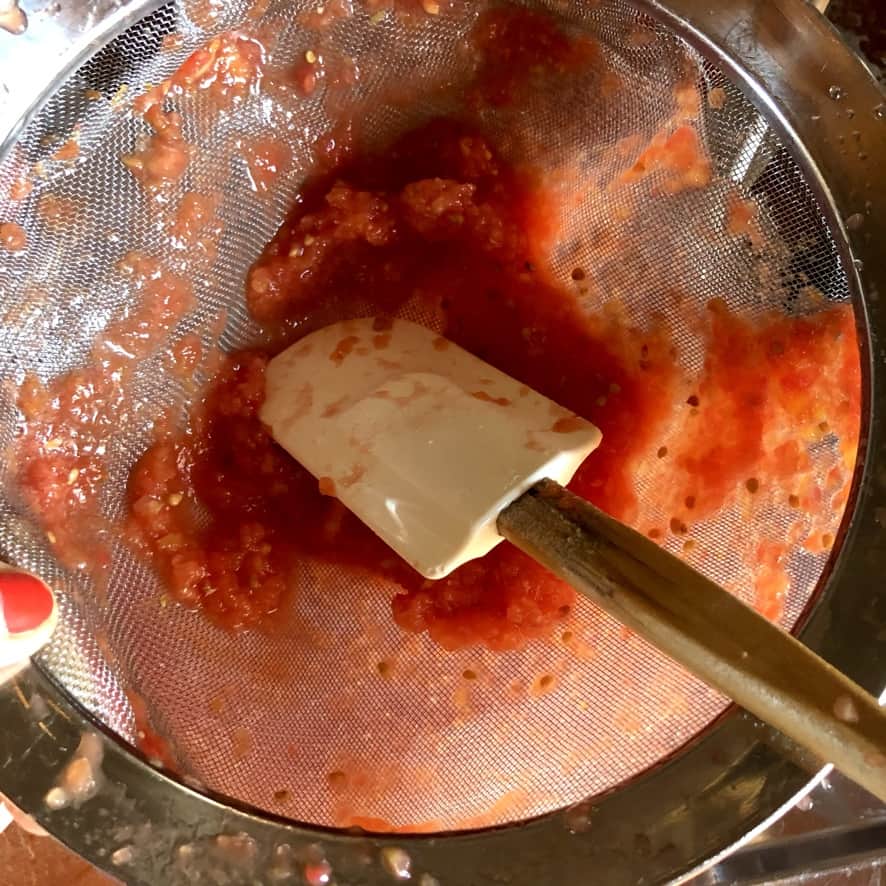 pressing pureed tomatoes through a fine mesh sieve using a rubber spatula