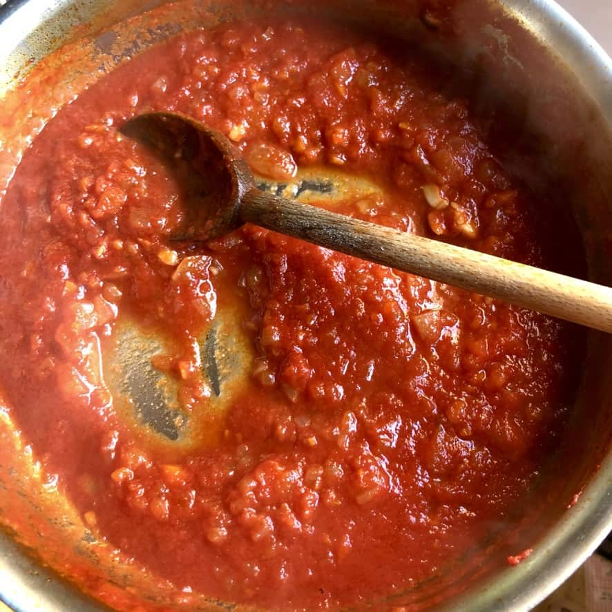 tomato and vegetable stirred together in the saute pan with a wooden spoon showing the final thickened stage the sauce should be in before using it in the parmigiana