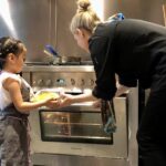 Kelly helping a super young kid get her dish into the oven to bake.