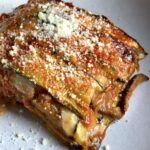 a large square of eggplant and zucchini parmigiana on a plate with grated cheese sprinkled on top