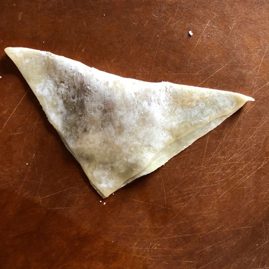 raw and filled wonton dough formed into a triangle before being formed into the final wonton shape