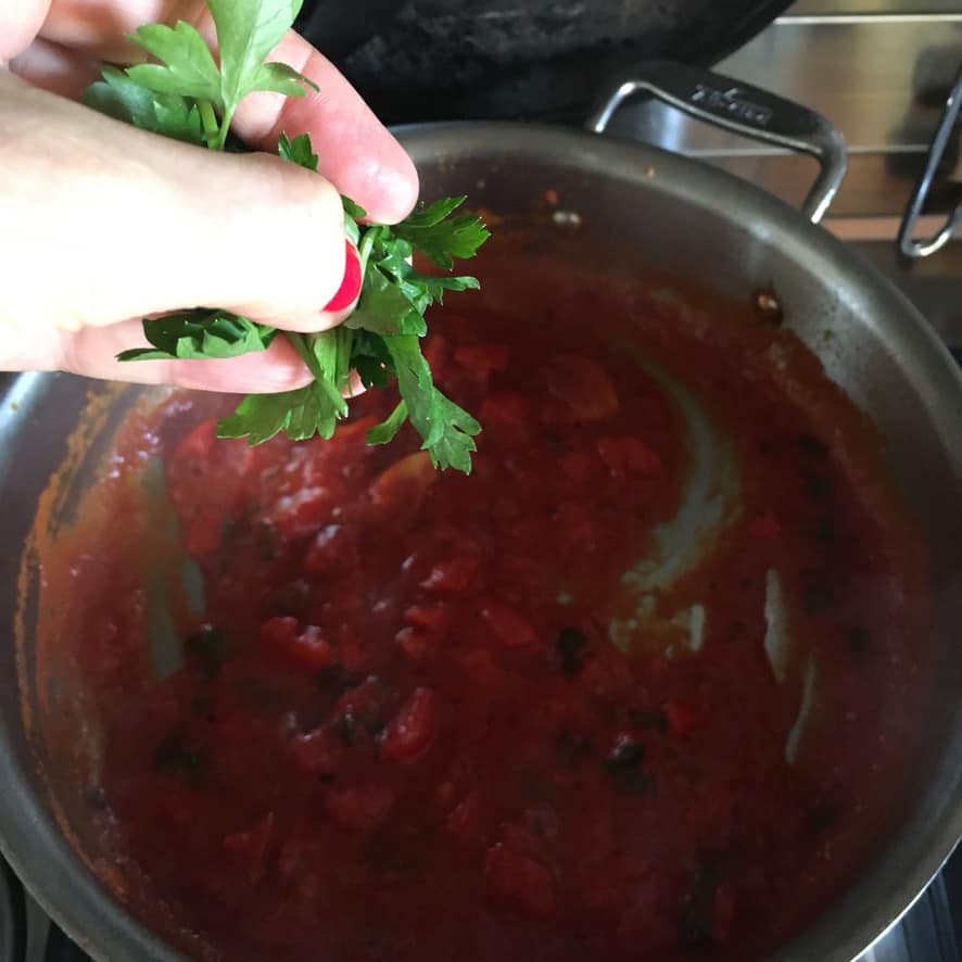 adding tomatoes and parsley to the hot pan