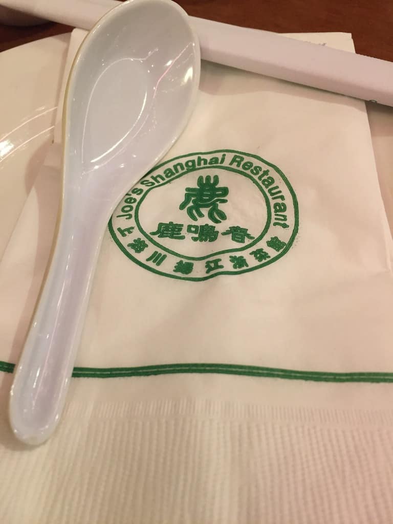 a simple white paper napkin with an Asian soup spoon lying on it with the Joe's Shanghai logo printed in Kelly green