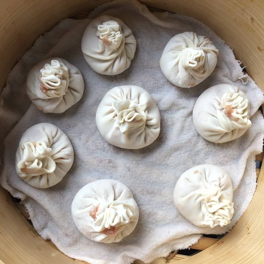 full view imperfectly pleated but still beautiful plump raw soup dumplings in a bamboo steamer