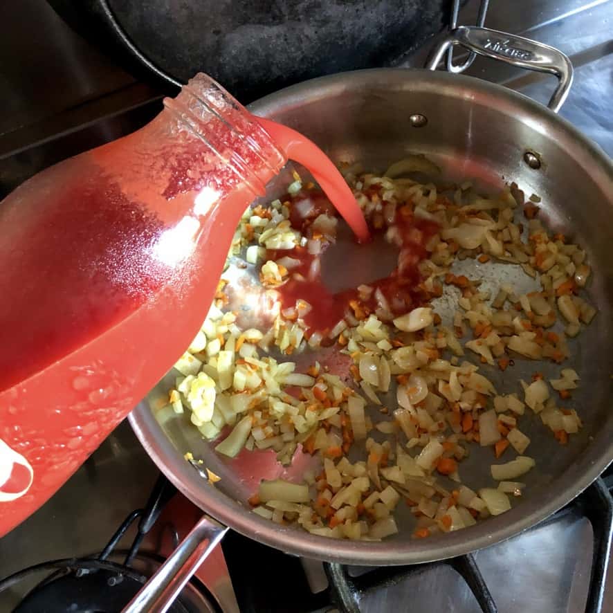 pouring homemade tomato puree into the onion mixture