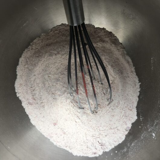 a whisk resting in the bowl after mixing the strawberry powder with the flour mixture