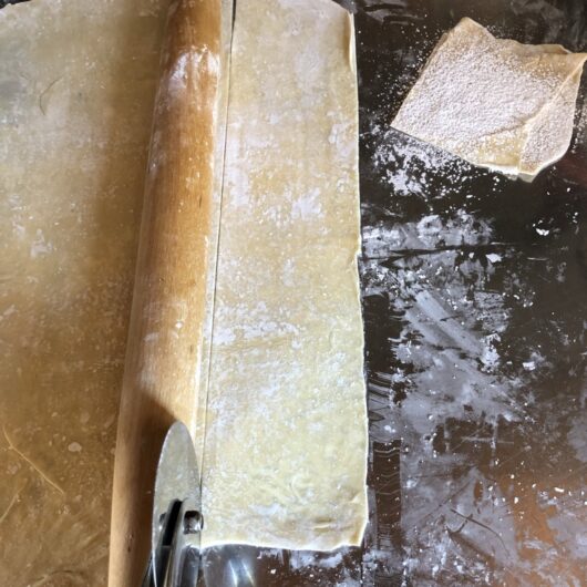 using the rolling pin as a guide to cut straight lines to make squares of wonton wrappers